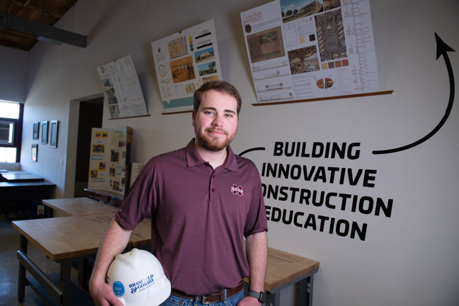 Jack Blacklock poses in MSU BCS studio holding Brasfield and Gorrie hard hat