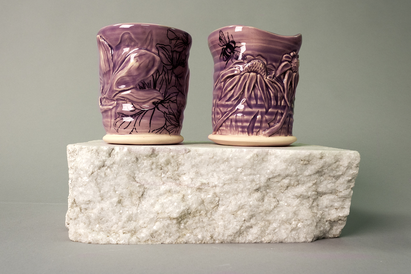 Purple cups carved with carved flowers sitting on a white stone.