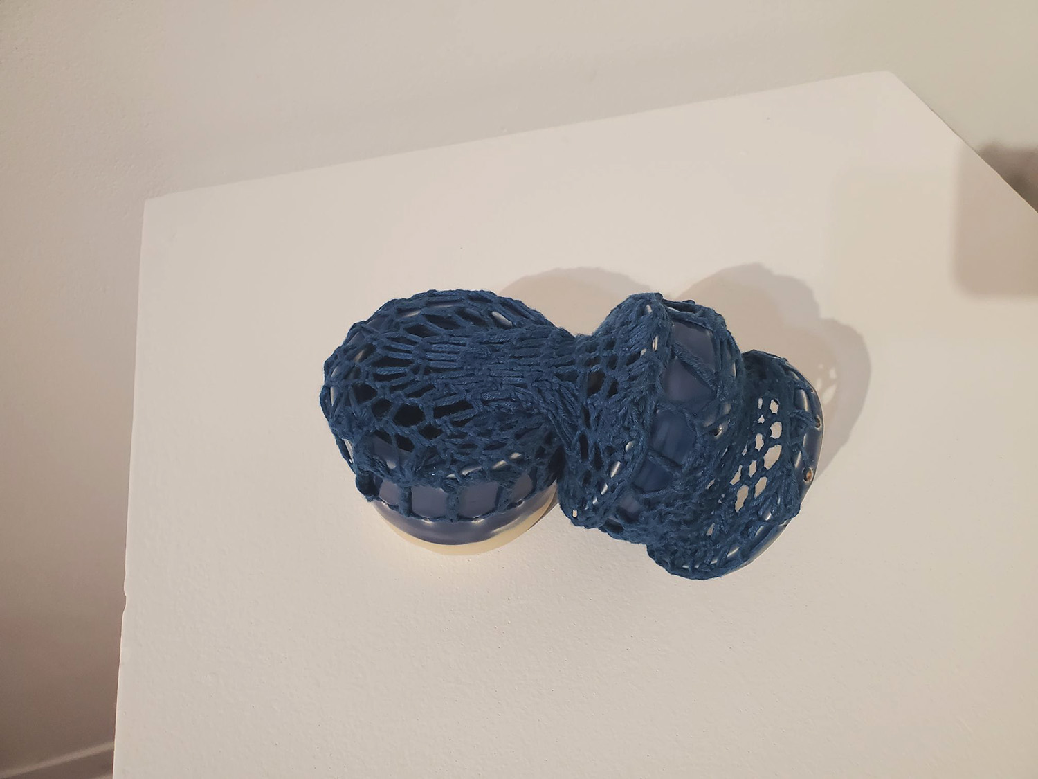 A blue cylinder broken and pieced together by blue yarn.