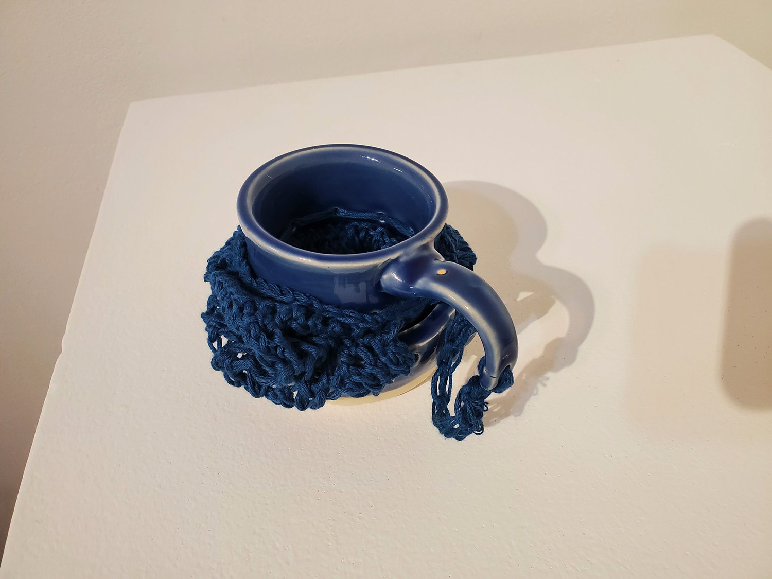A blue mug broken and pieced together by blue yarn.