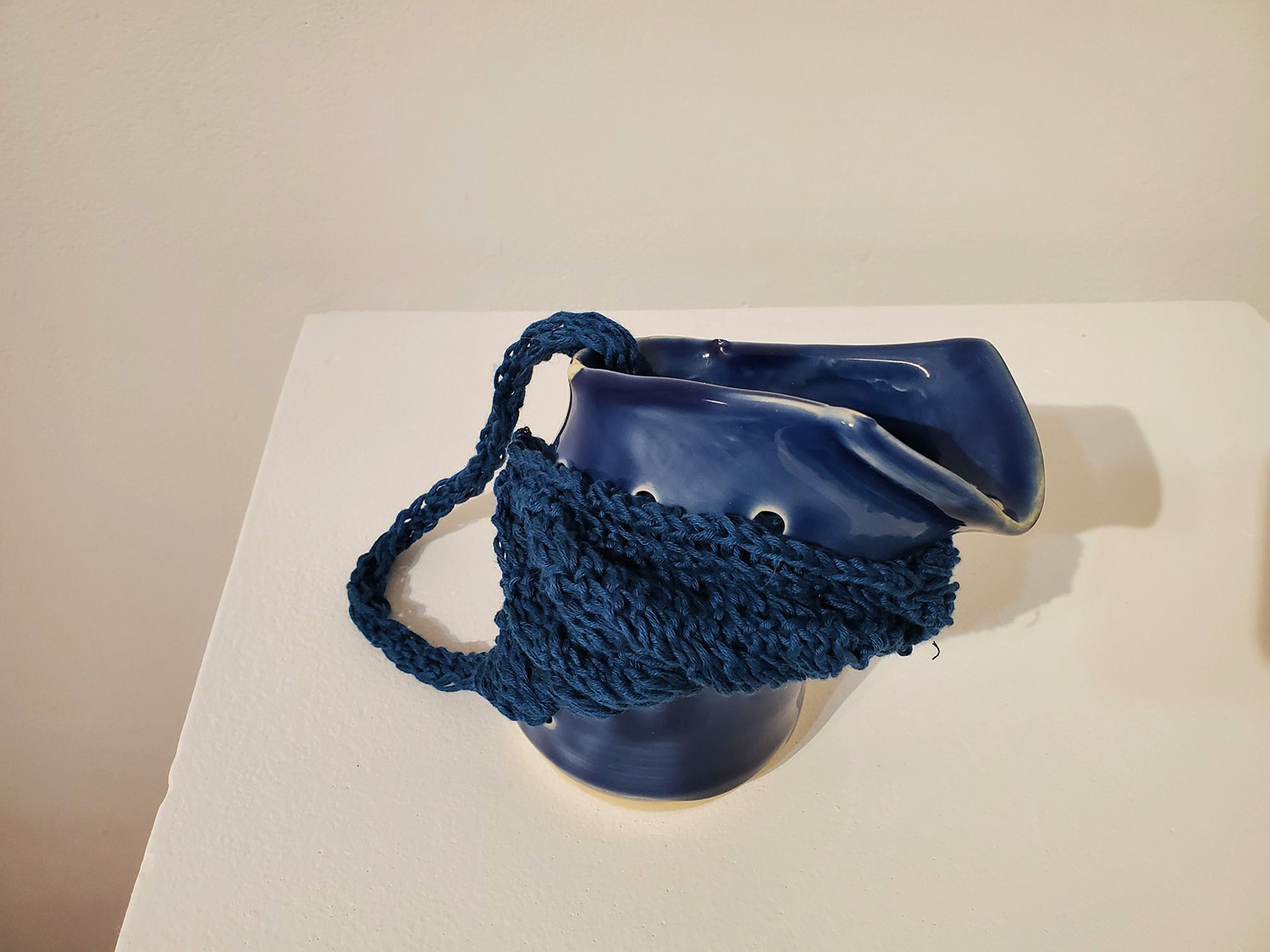 A blue pitcher broken and pieced together by blue yarn. 