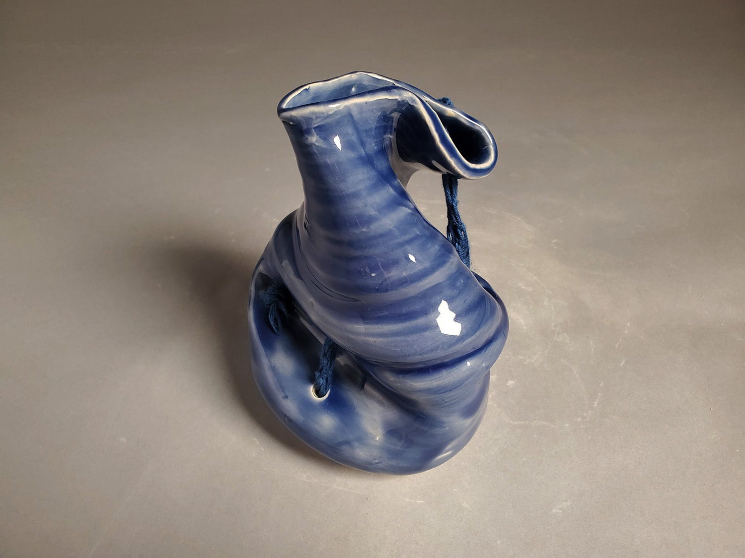 A blue wide cylinder twisted with one end wrapped downwards. 