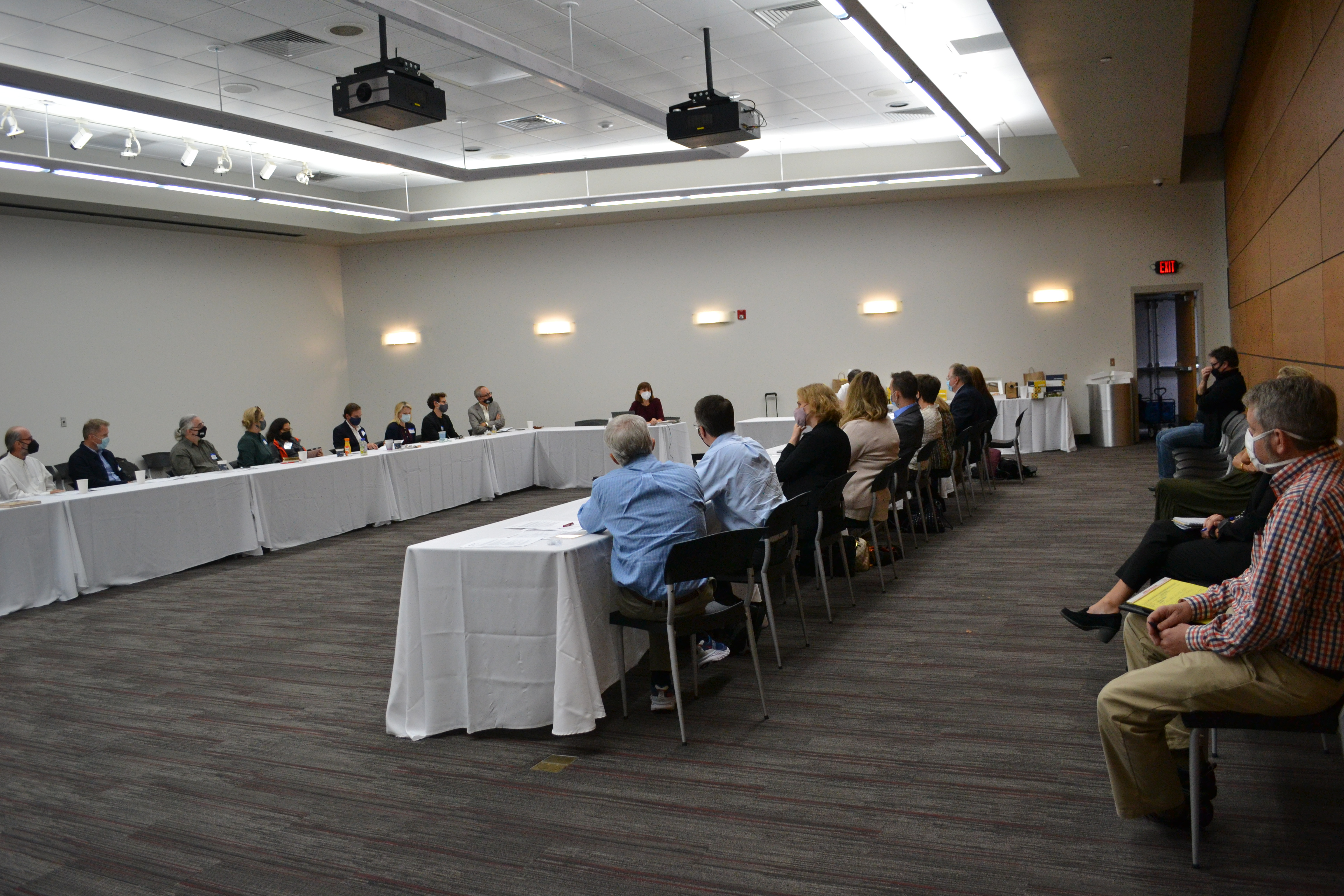 Advisory Board members sit around large open rectangle table, some sit in chairs along edge of room