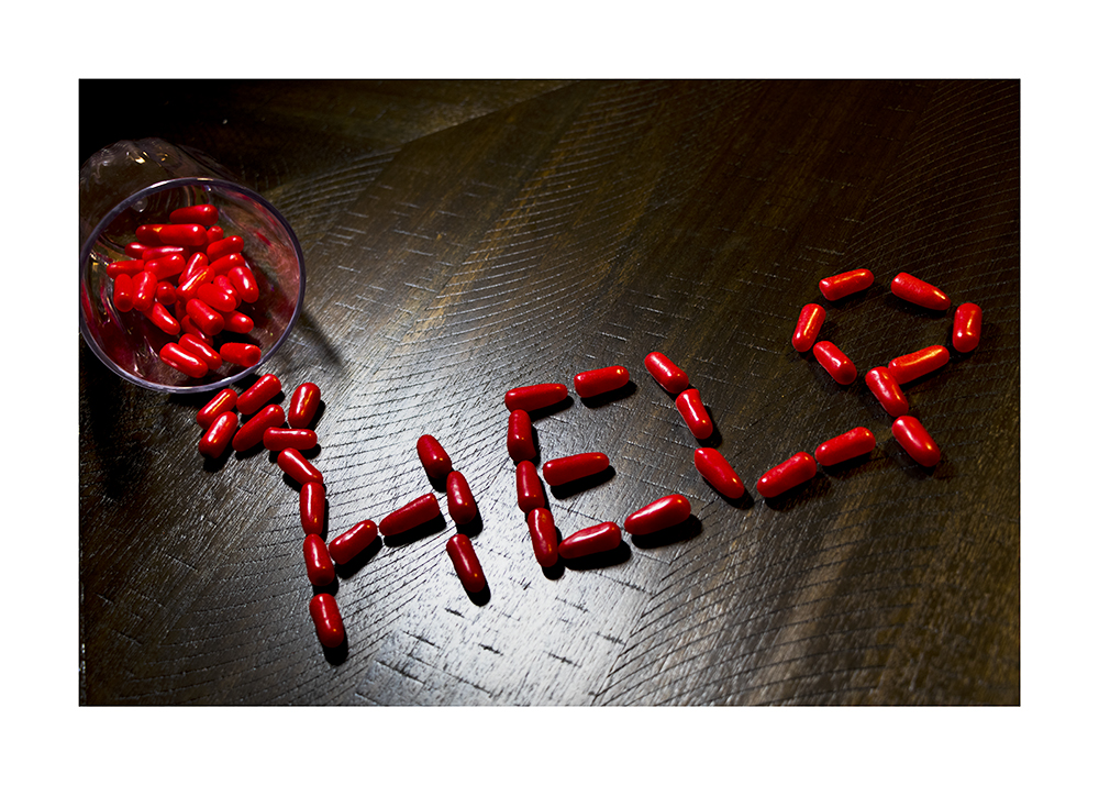 A photograph of red pills spilt on a table spelling out the word "Help"