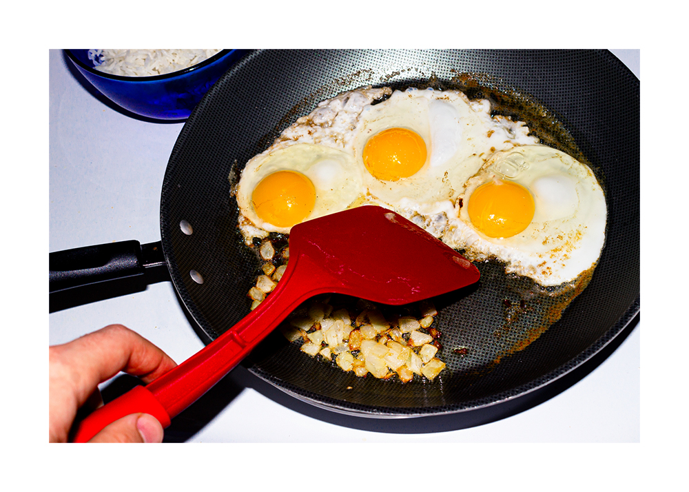 A photograph of someone scrambling eggs in a pan using a red spatula