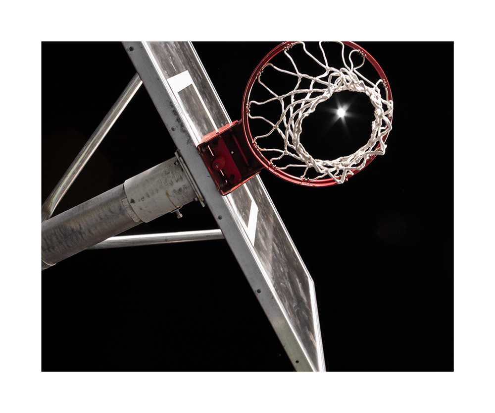 A photograph of a basketball goal from dog eyes view with the moon shining through at night
