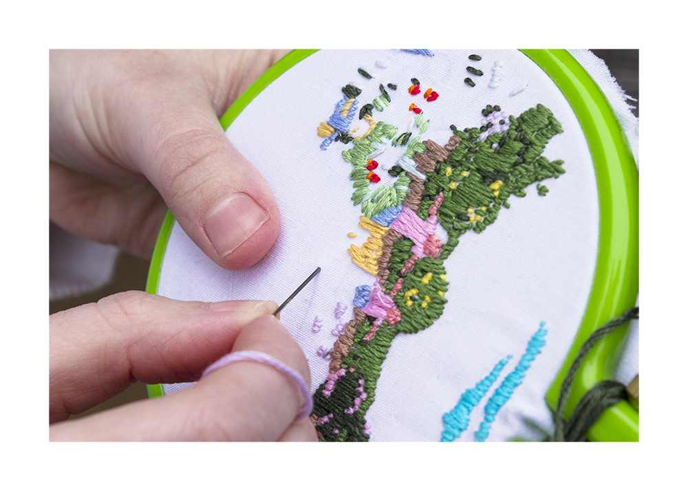 A photograph of someone sewing something using the colors green, blue, yellow, and light purple.