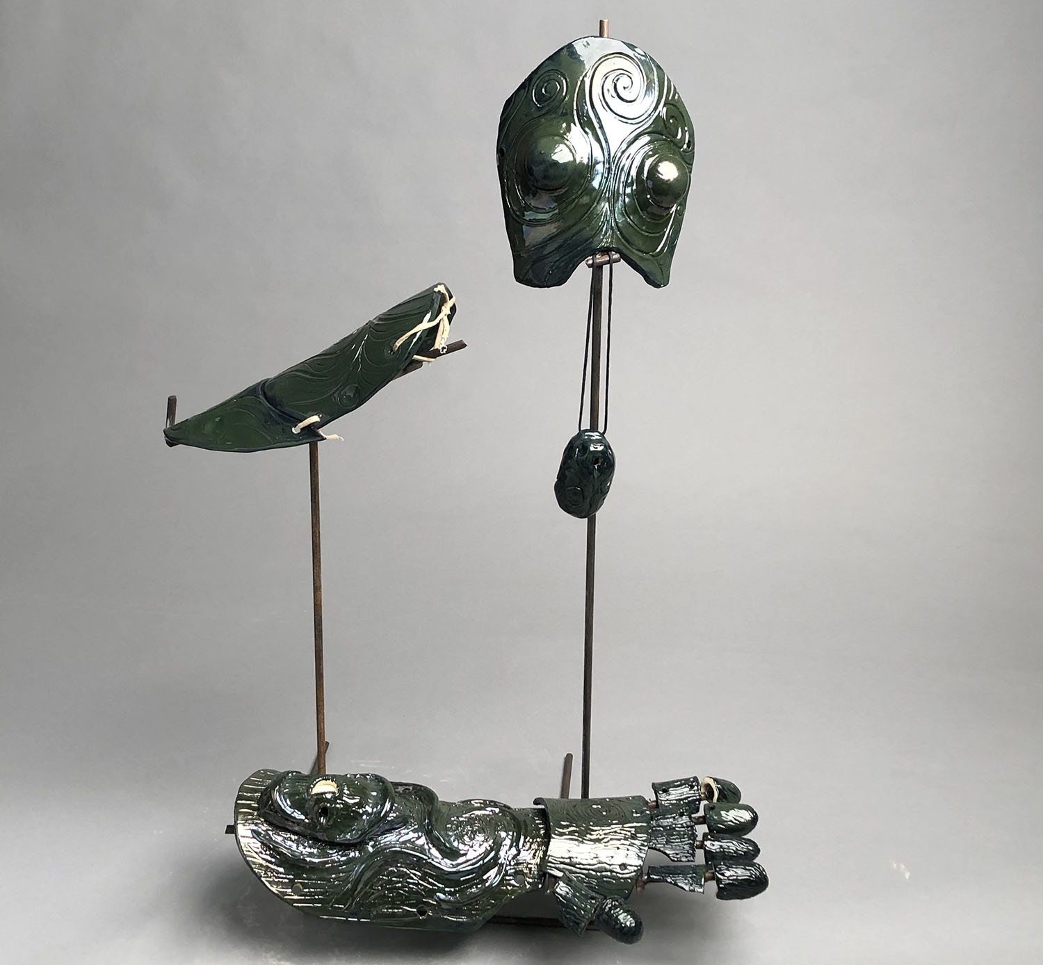 Metal frame supporting ceramic armor pieces with head, shoulder, arm and hand piece with iridescent green glaze and swirling pattern designs. 