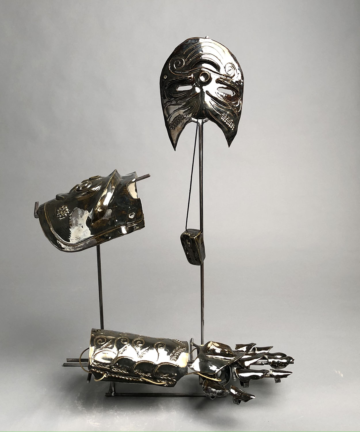 Metal frame supporting ceramic armor pieces with head, shoulder, arm and hand piece with metallic glaze, engravings, and designs. 