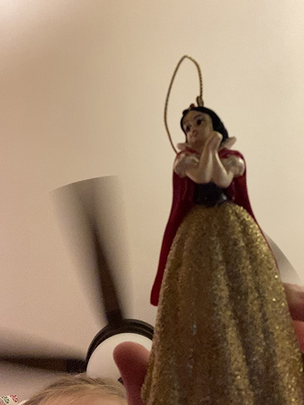 Photograph of a princess Christmas ornament held up under a ceiling fan.
