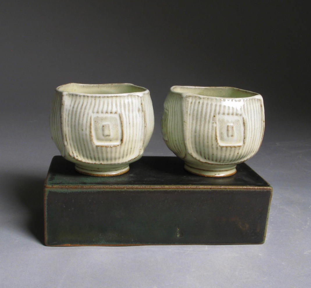 Two white ceramic cups on a dark ceramic brick.