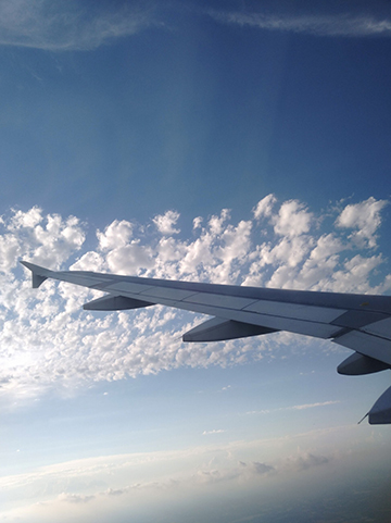 Photograph of the sky with clouds and an airplane wing taken from an airplane window.