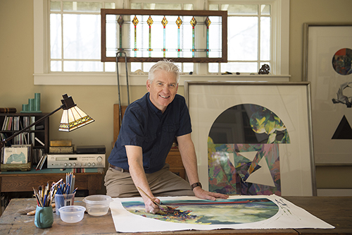 Brent Funderburk leans over desk and painting in his studio.