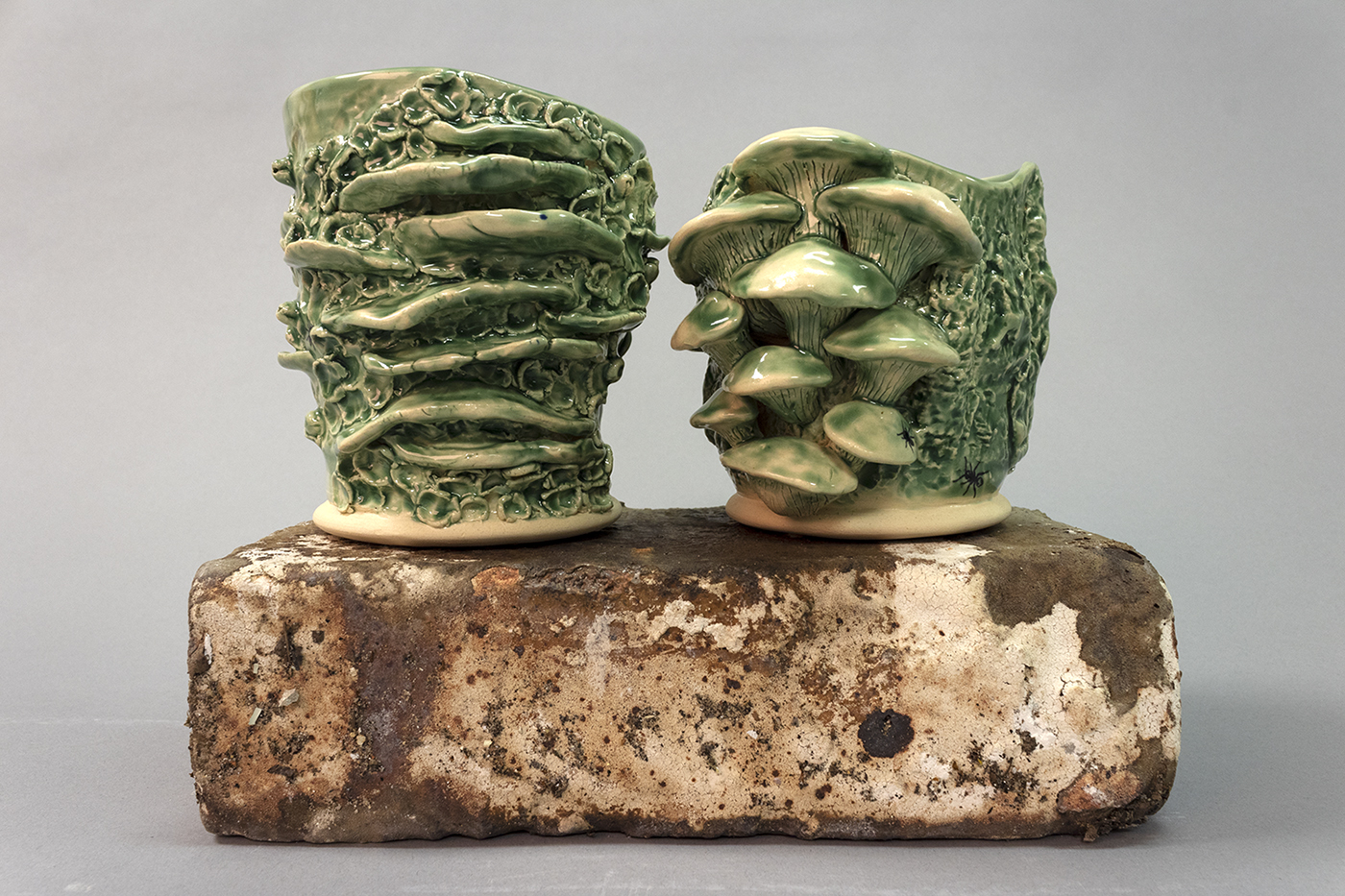 Two cups with mushrooms carved and sculpted with green glaze.  Sitting on a brick.