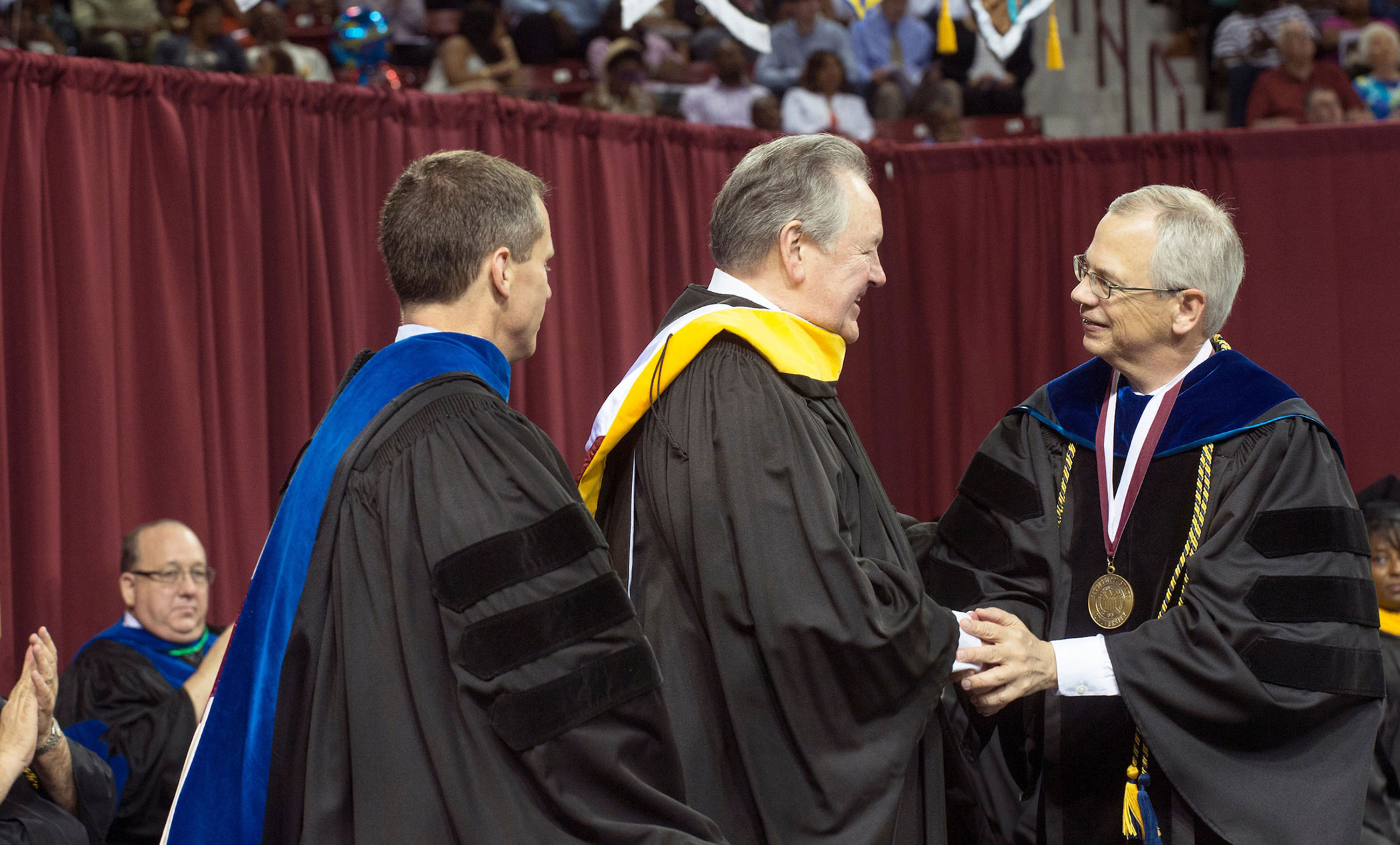 Bob Harrison, center, shakes hands with the provost, right, wearing graduation garb
