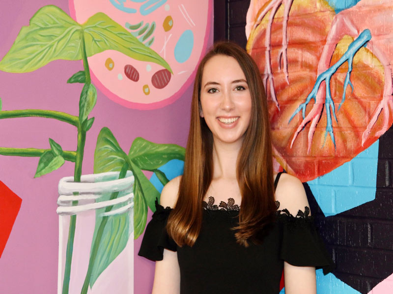 Hanna Bewley standing in front of her mural in Harned Hall.
