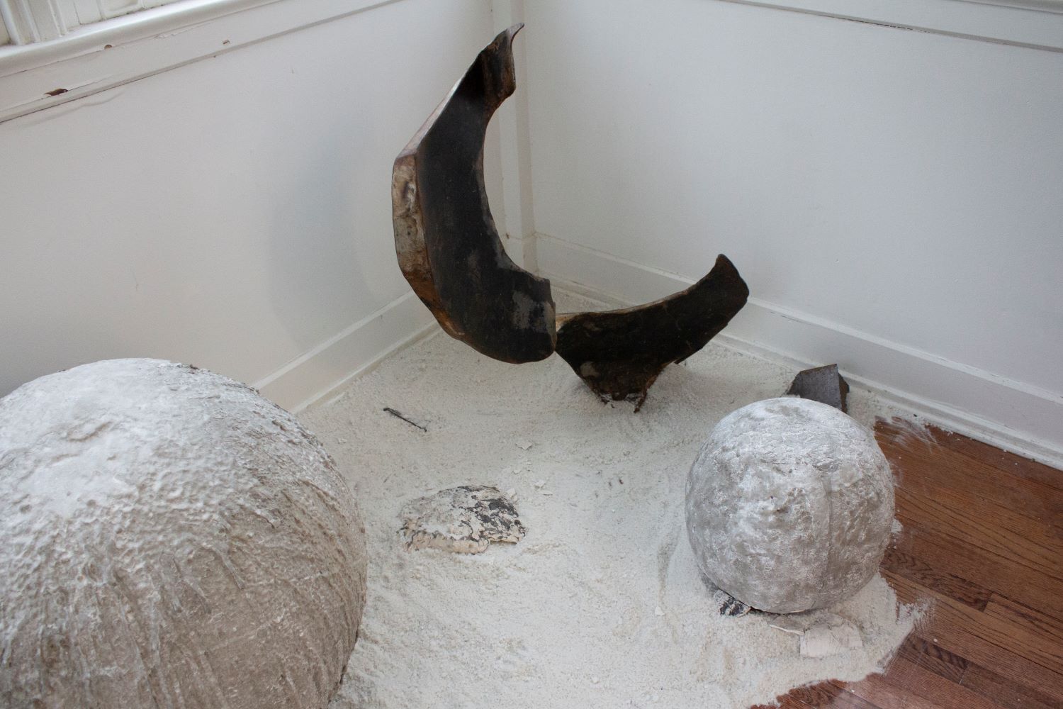 large metal sculpture and 2 concrete orbs sitting on sand