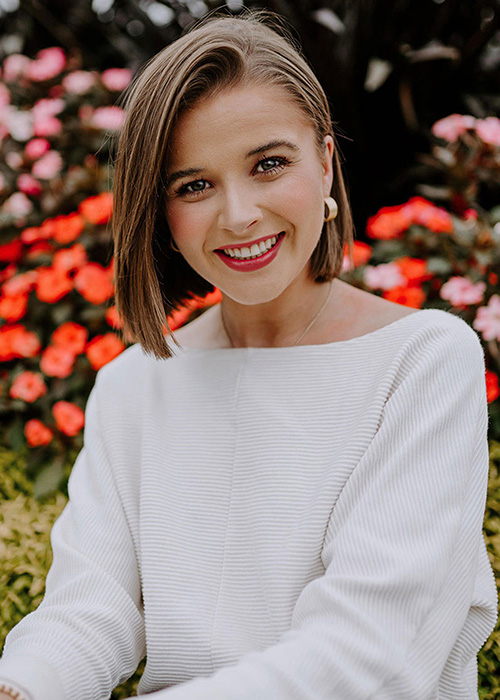 Hayden Hunt wearing white poses with red flowers in background