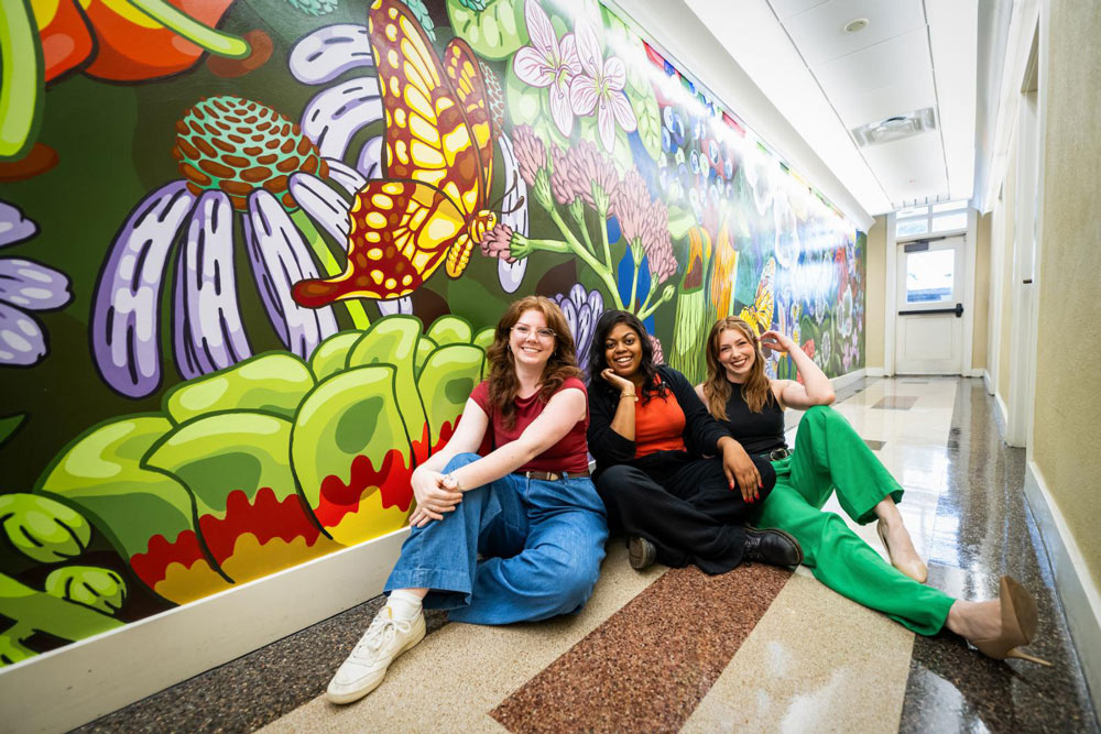 From left, MSU graduate Mary Sanders, of Starkville, senior art major Sarah Demus of Jackson, and May graduate Sadie “Bella” Brownlee of Louisville, stand in front their completed artwork.