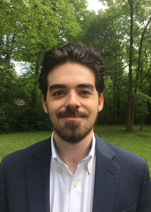 Matthew Hudgins in suit jacket outside - green grass and trees in background