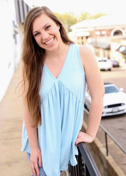 Baleigh Hull poses in light blue shirt with downtown Starkville in background