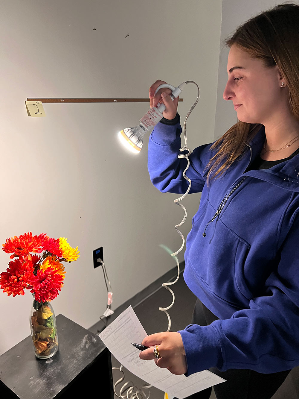 student shines light on flower on table in lighting lab