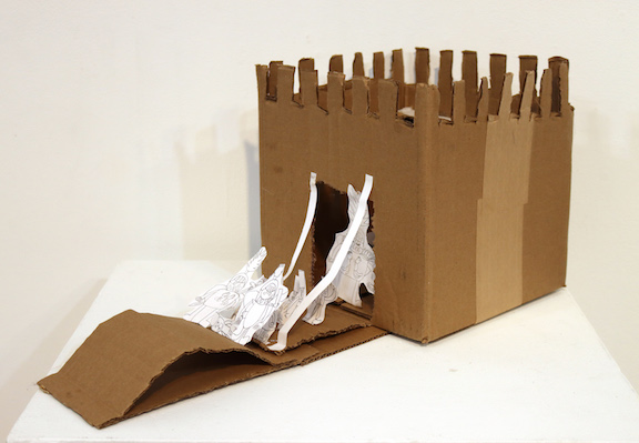 A cardboard diorama of a castle and draw bridge with paper people walking across the bridge.