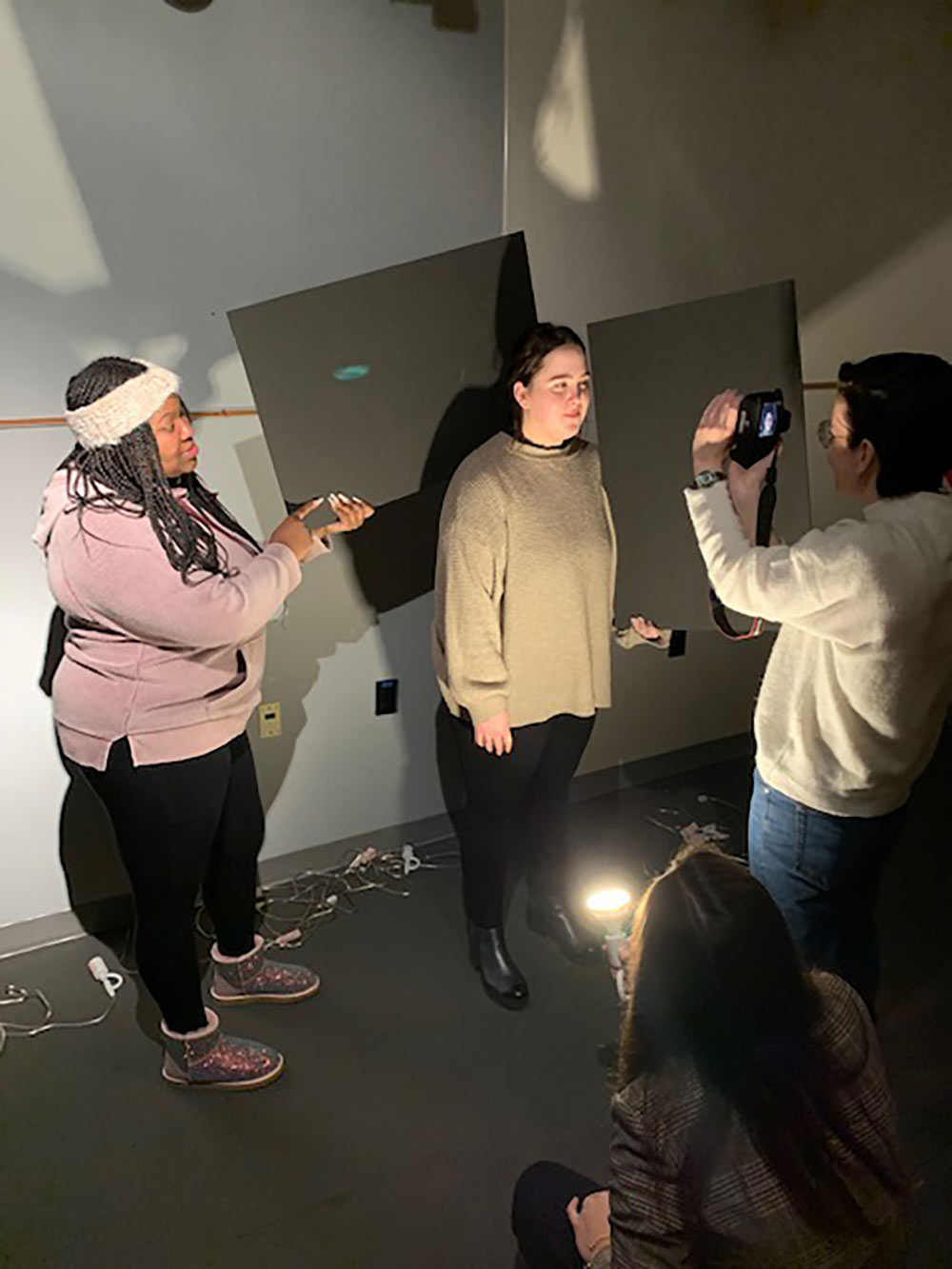 4 students shown in small space with lights. One students is taking a photo