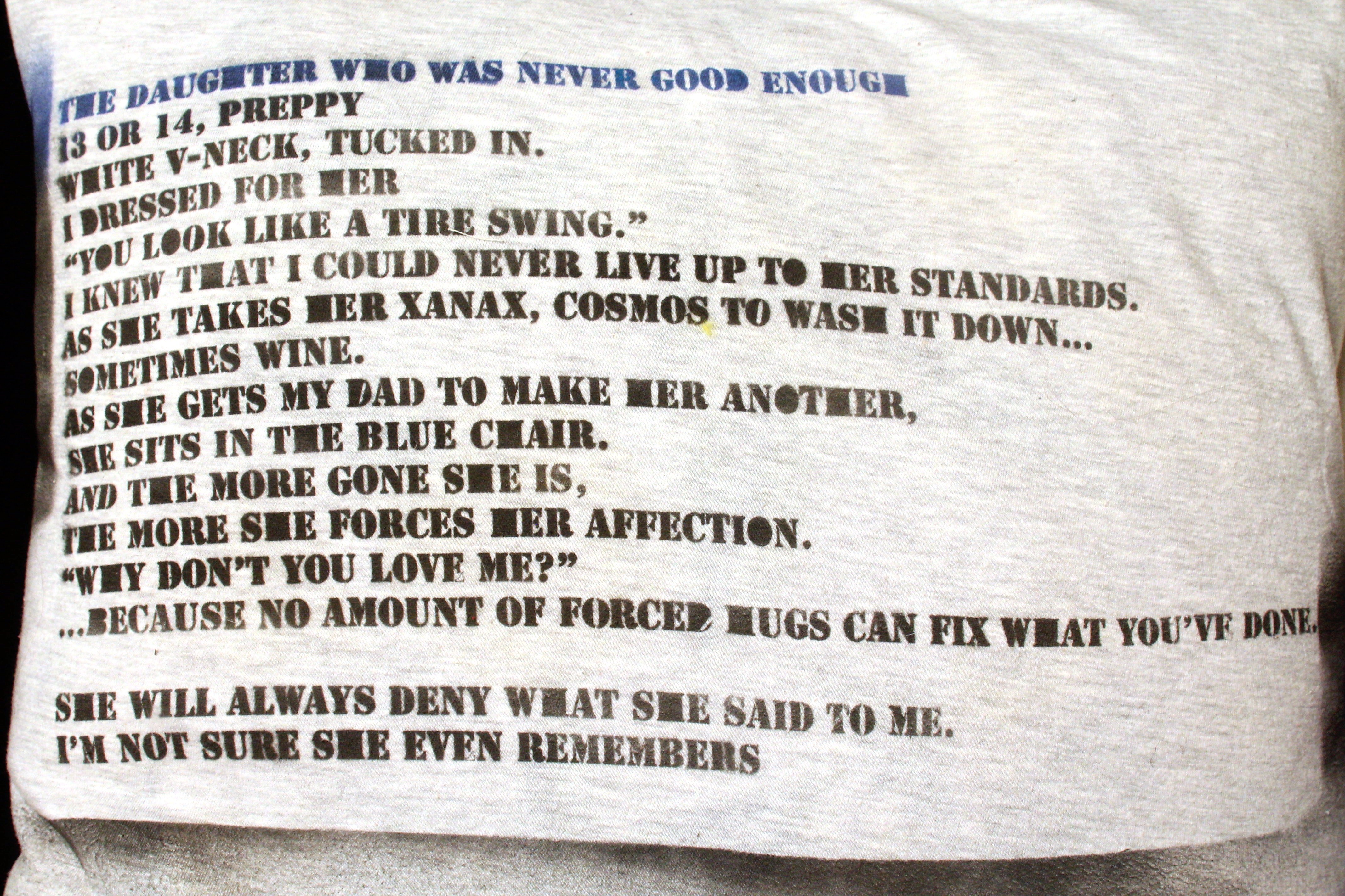 poem on pillow: THE DAUGHTER WHO WAS NEVER GOOD ENOUGH 13 OR 14, PREPPY WHITE V-NECK, TUCKED IN. I DRESSED FOR HER “YOU LOOK LIKE A TIRE SWING.” I KNEW THAT I COULD NEVER LIVE UP TO HER STANDARDS. AS SHE TAKES HER XANAX, COSMOS TO WASH IT DOWN… SOMETIMES WINE. AS SHE GETS MY DAD TO MAKE HER ANOTHER, SHE SITS IN THE BLUE CHAIR. AND THE MORE GONE SHE IS, THE MORE SHE FORCES HER AFFECTION. “WHY DON’T YOU LOVE ME?” ...BECAUSE NO AMOUNT OF FORCED HUGS CAN FIX WHAT YOU’VE DONE.  SHE WILL ALWAYS DENY WHAT SHE SAID TO ME. I’M NOT SURE SHE EVEN REMEMBERS