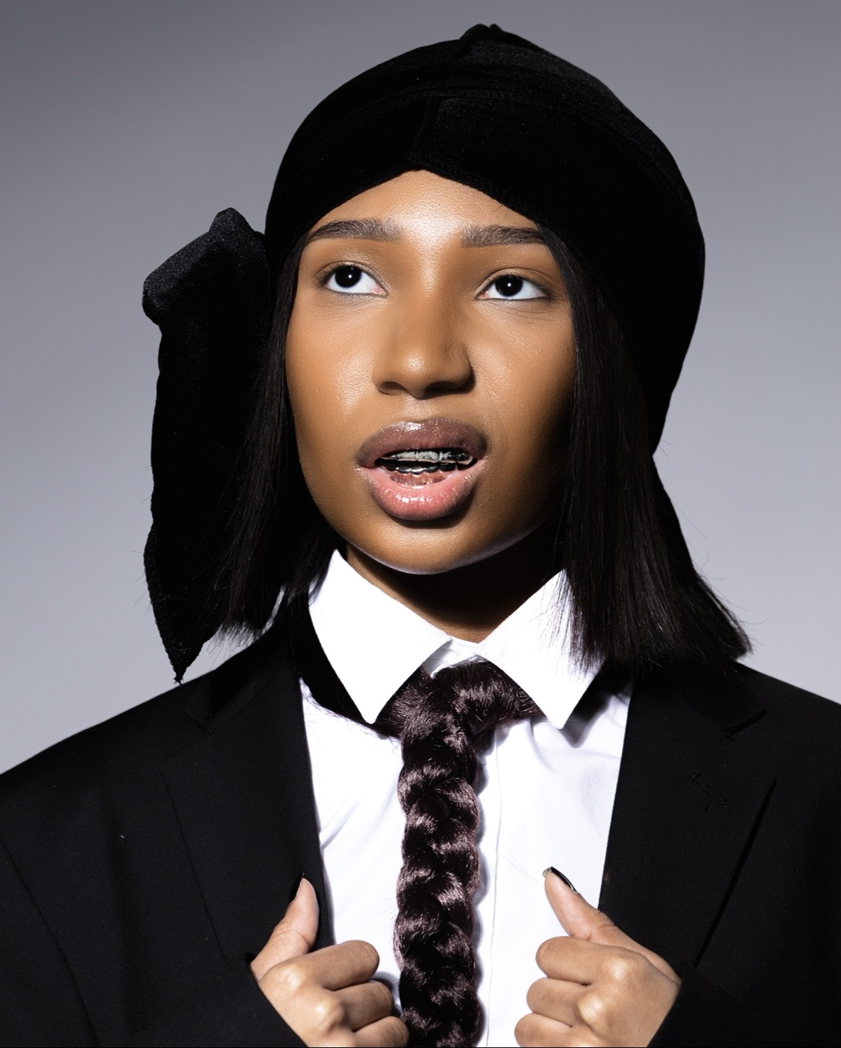 Photo by Jahari Bell from his "A Man's World" series shows a woman wearing a black suit with a braided hair tie looking to the top left