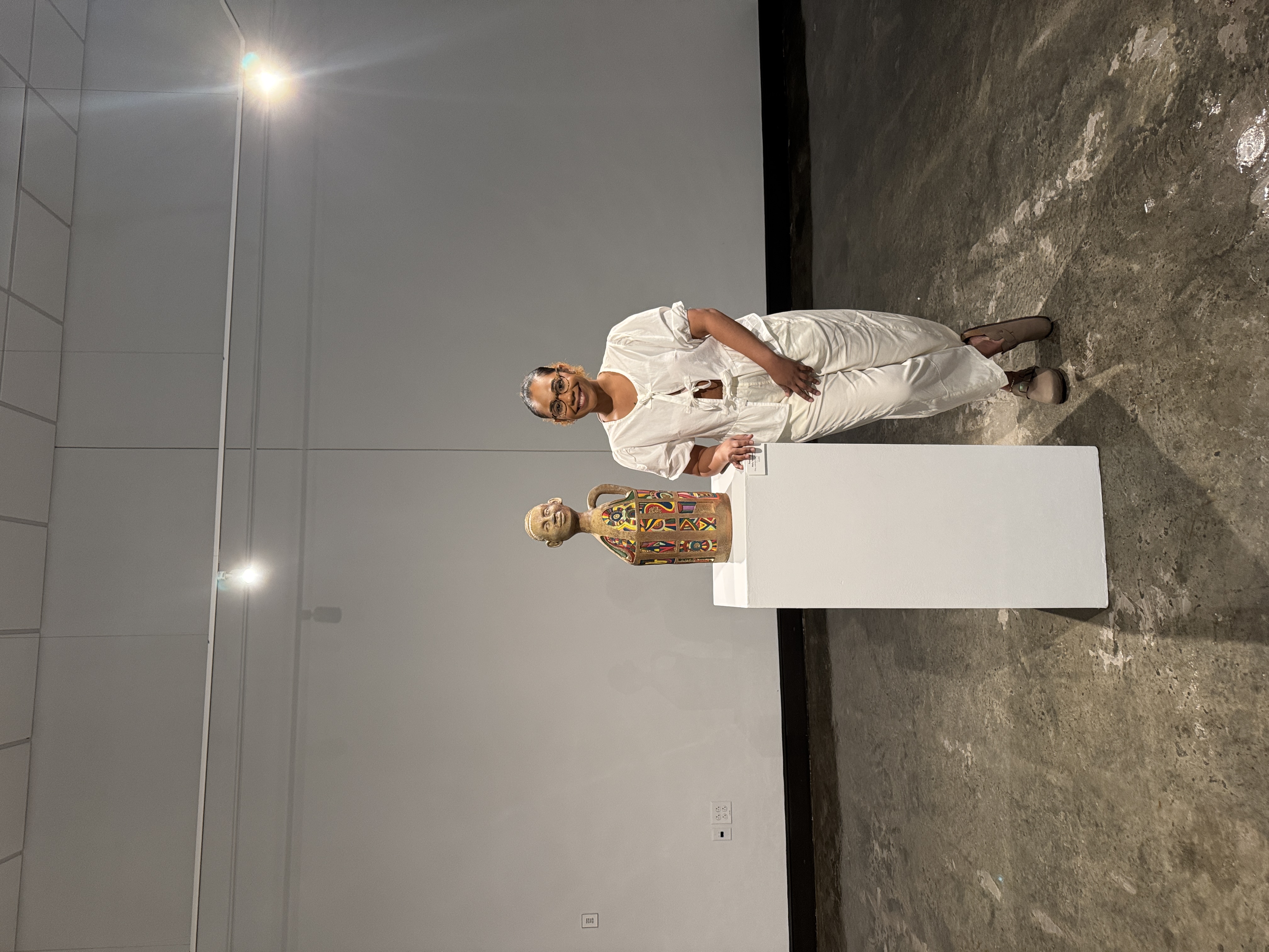 Artist Lexus Giles poses with one of her clay sculptures in her exhibit, "Record Keeper: Testament to Resilience," located in the Old Main Gallery.