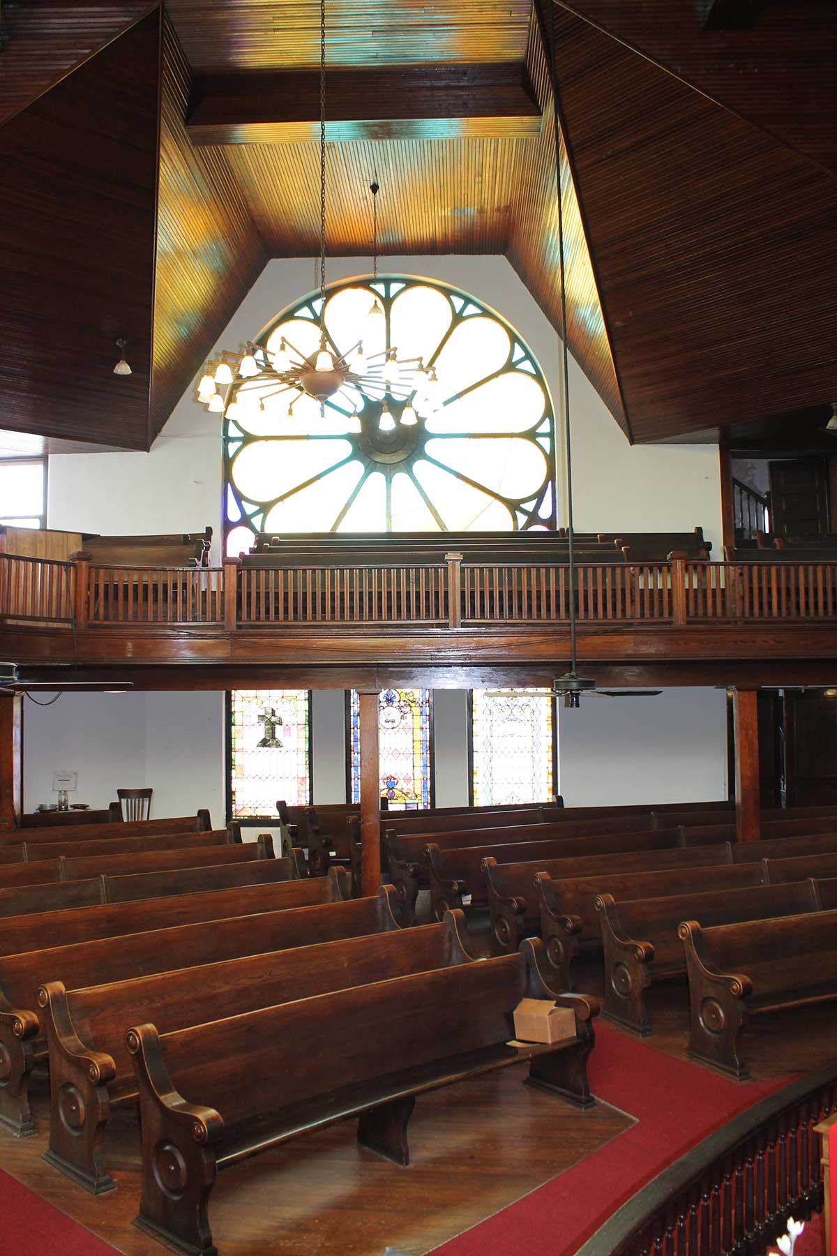 church interior shows wooden pews and stained glass window at back