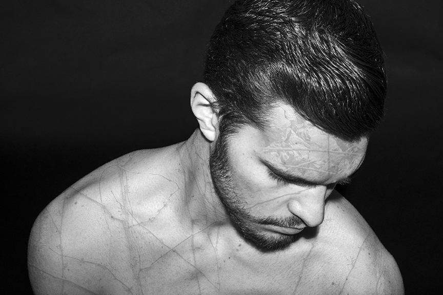 Black and white photograph of shirtless male figure looking down.