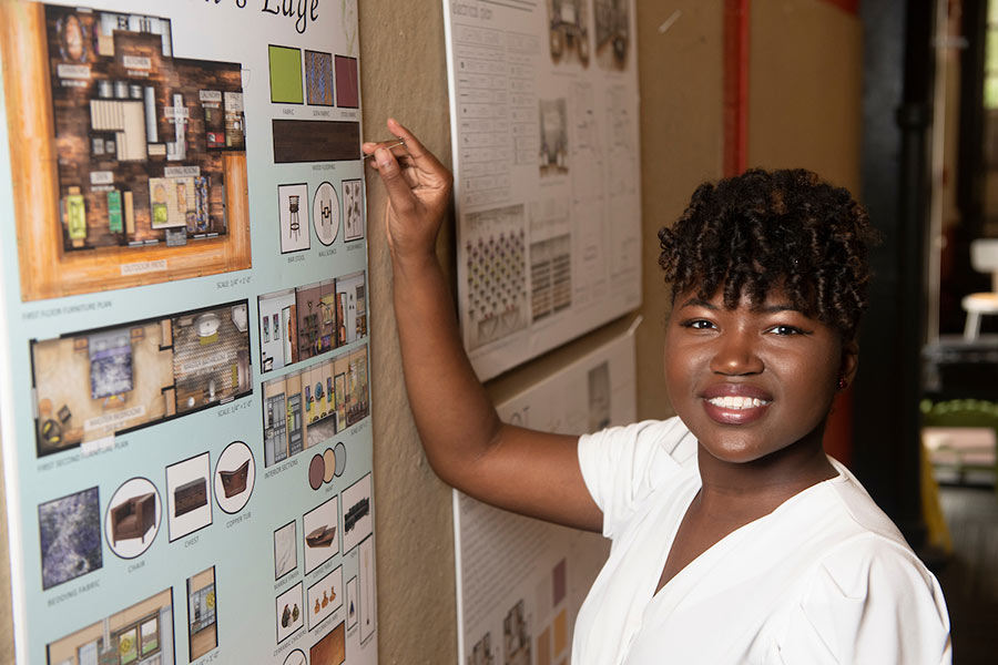 student Onjellica Harris stand in front of interior design work hanging at left