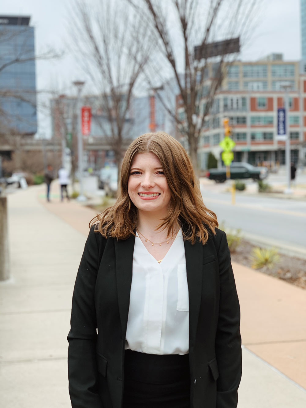 Katelyn Courtney stands in black suit with street and city scenery behind her