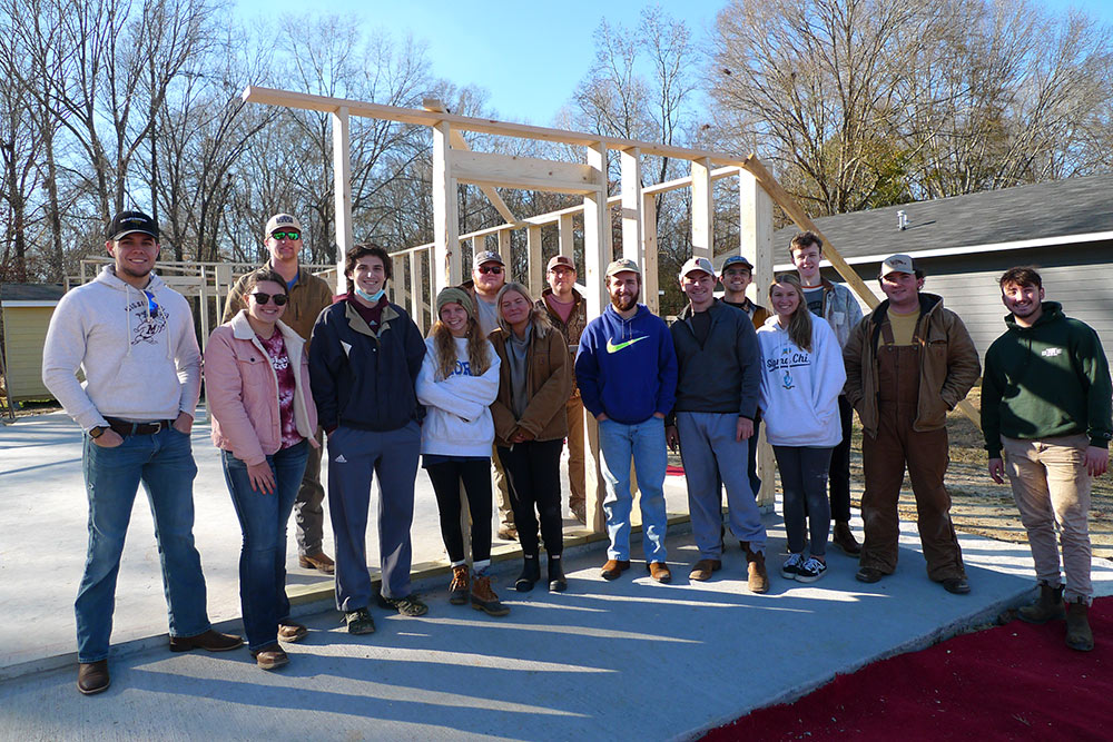 group poses on concrete slab with wood framing behind in house under construction