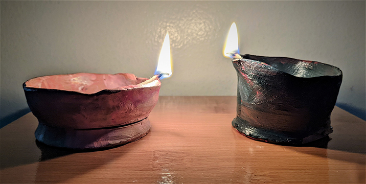 Two clay lamps with match flames resting on the edge of each.