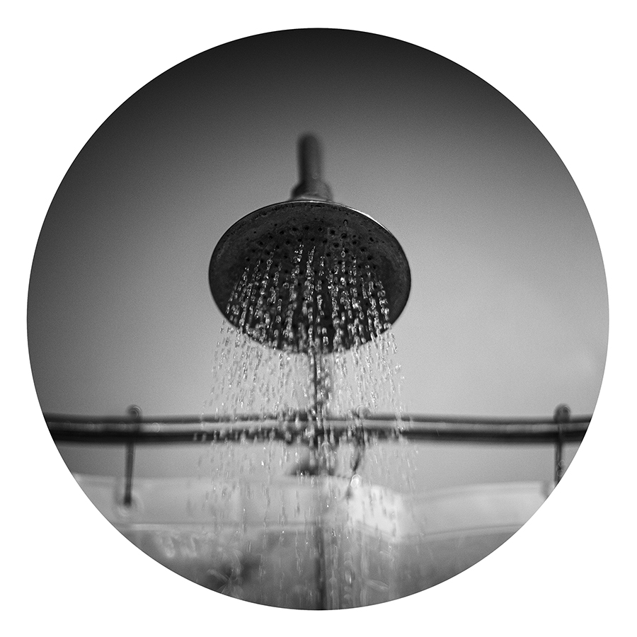 Black and white photograph of a shower head with water spraying out.