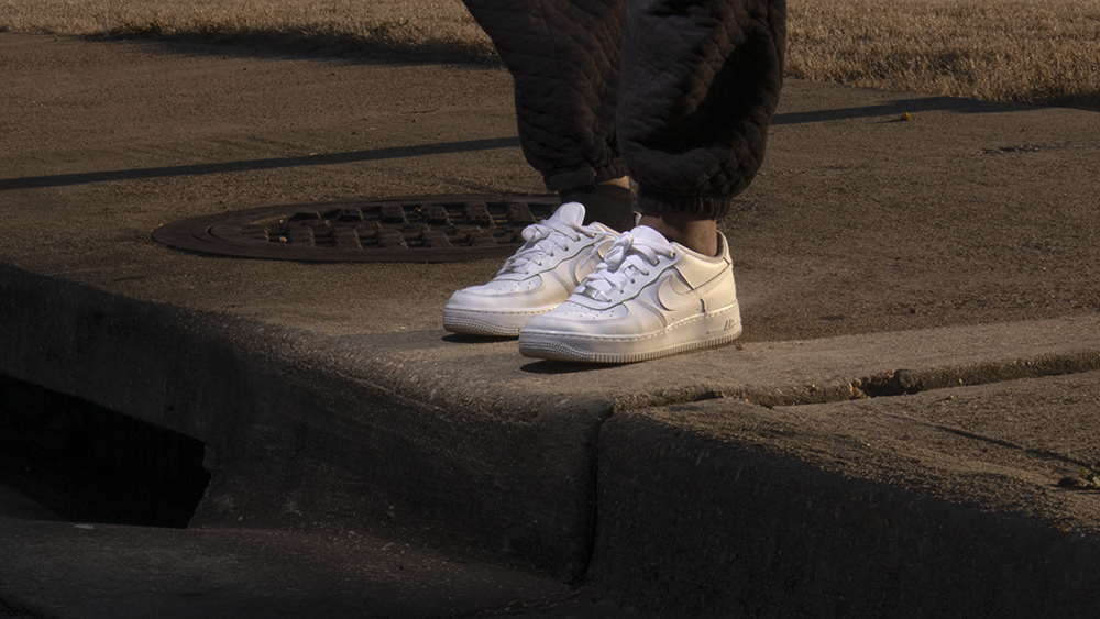 A photograph of a persons white shoes standing on the sidewalk