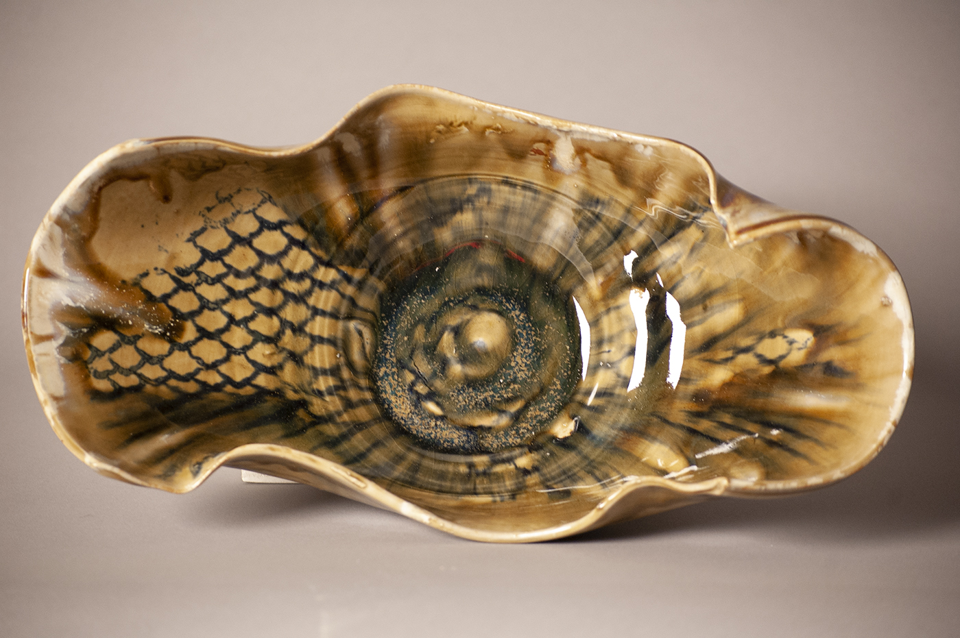 Amber green ceramic bowl with blue scale pattern and curling edge. 