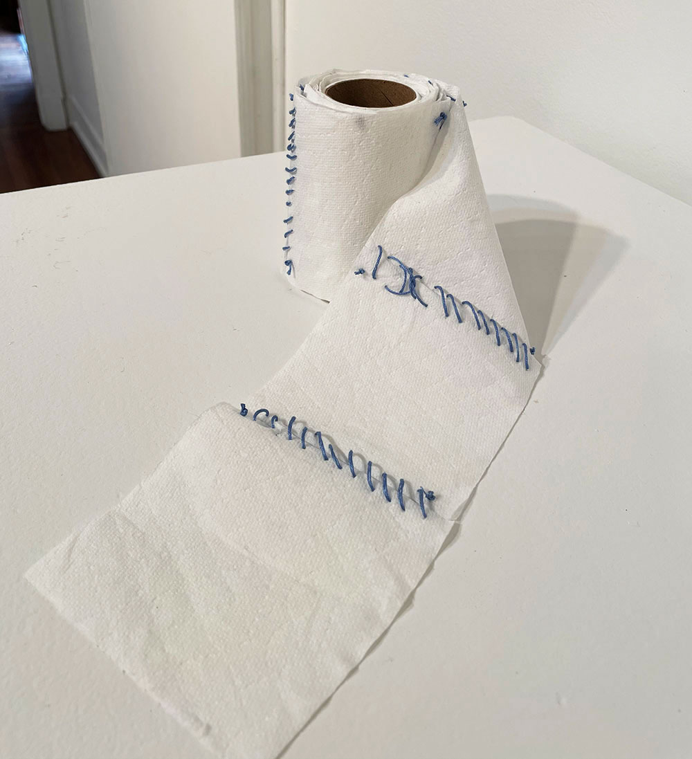 A roll of toilet paper sown back together on each square by blue thread