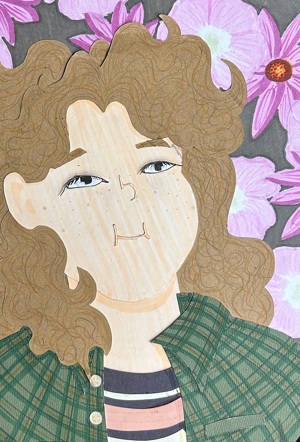 Close-up image of cut-paper portrait of a girl with brown hair, blue eyes, and freckles. She wears a green flannel and striped black, yellow, and pink shirt. The background features black eyed Susans and showy primrose. 