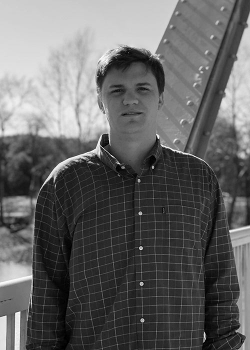 Black and white image of Evan McElwrath posing outside - bridge in background