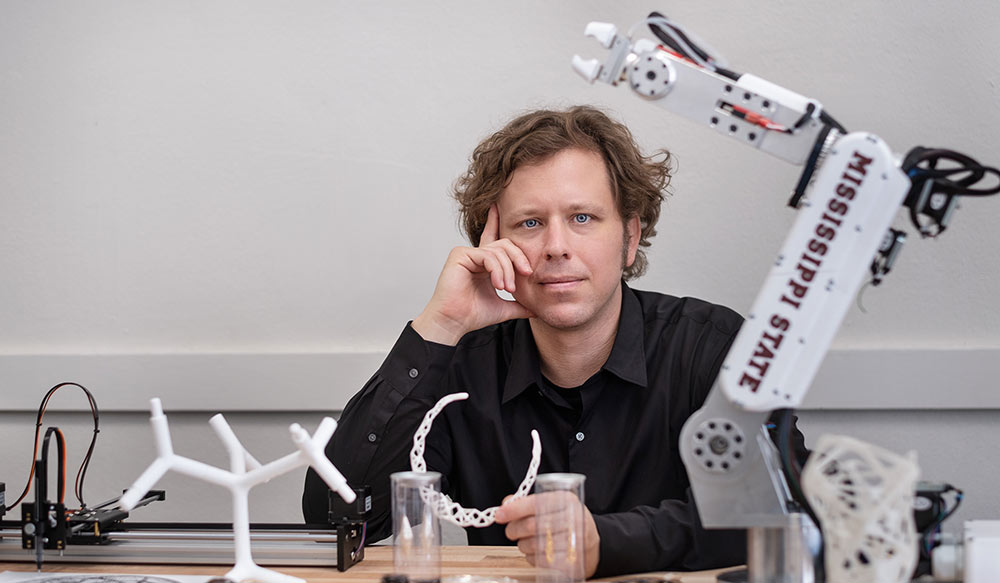 Duane McLemore poses with a robot and 3d printed material