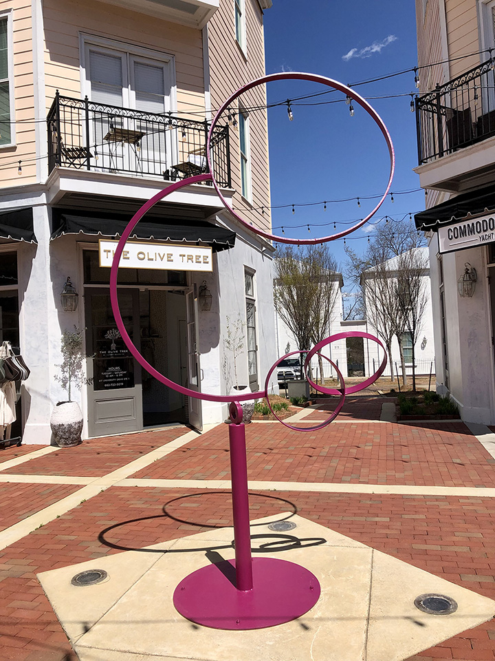 A metal statue painted pink in an outdoor shopping plaza.