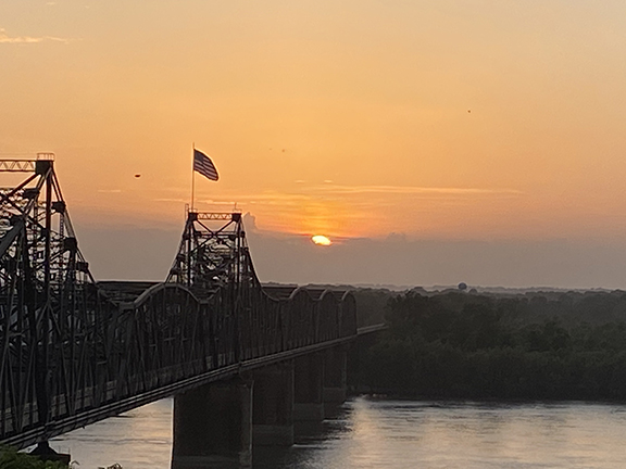 Color photograph of sunset landscape and a bridge over river.