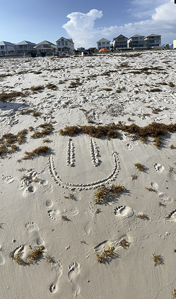 Photograph of a sandy beach with a smiley face drawn in the sand.