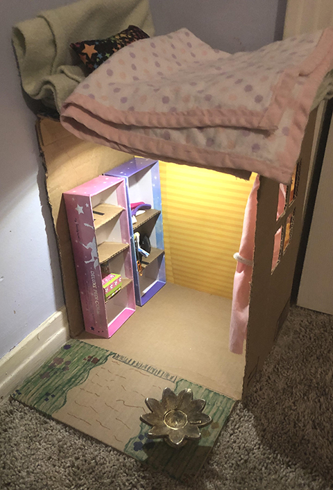 Photograph of a homemade dollhouse under a bed.