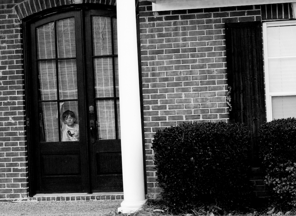 Photograph of a child in the window pane of a wooden door