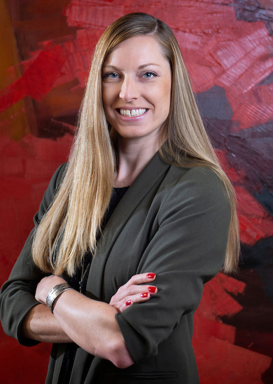 headshot of Lori Neuenfeldt - arms crossed, red painting background